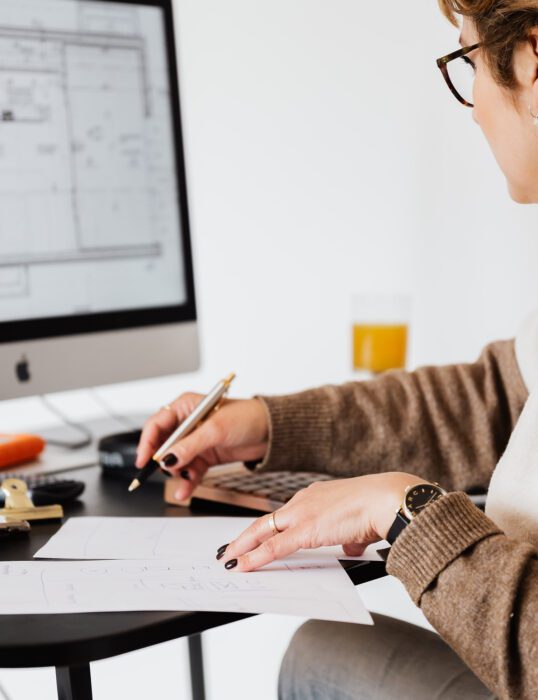 Woman at desk taking notes from a screen showing building plans